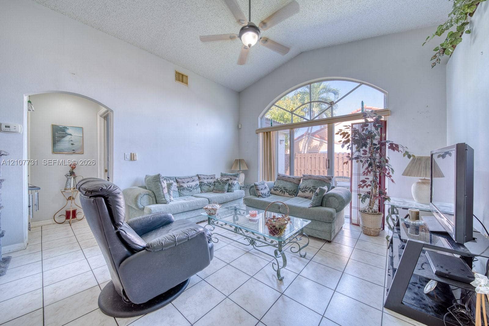 Vaulted ceilings, arched window, sliding glass door, and neutral ceramic tile flooring