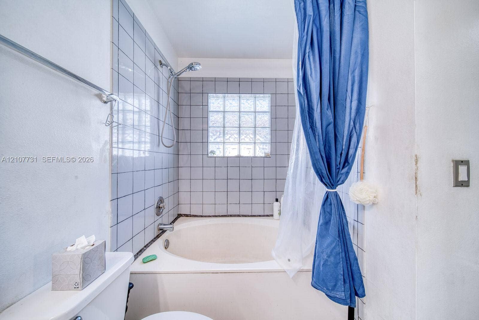 Deep soaking tub with a tiled surround, integrated shower fixture, and a glass block window