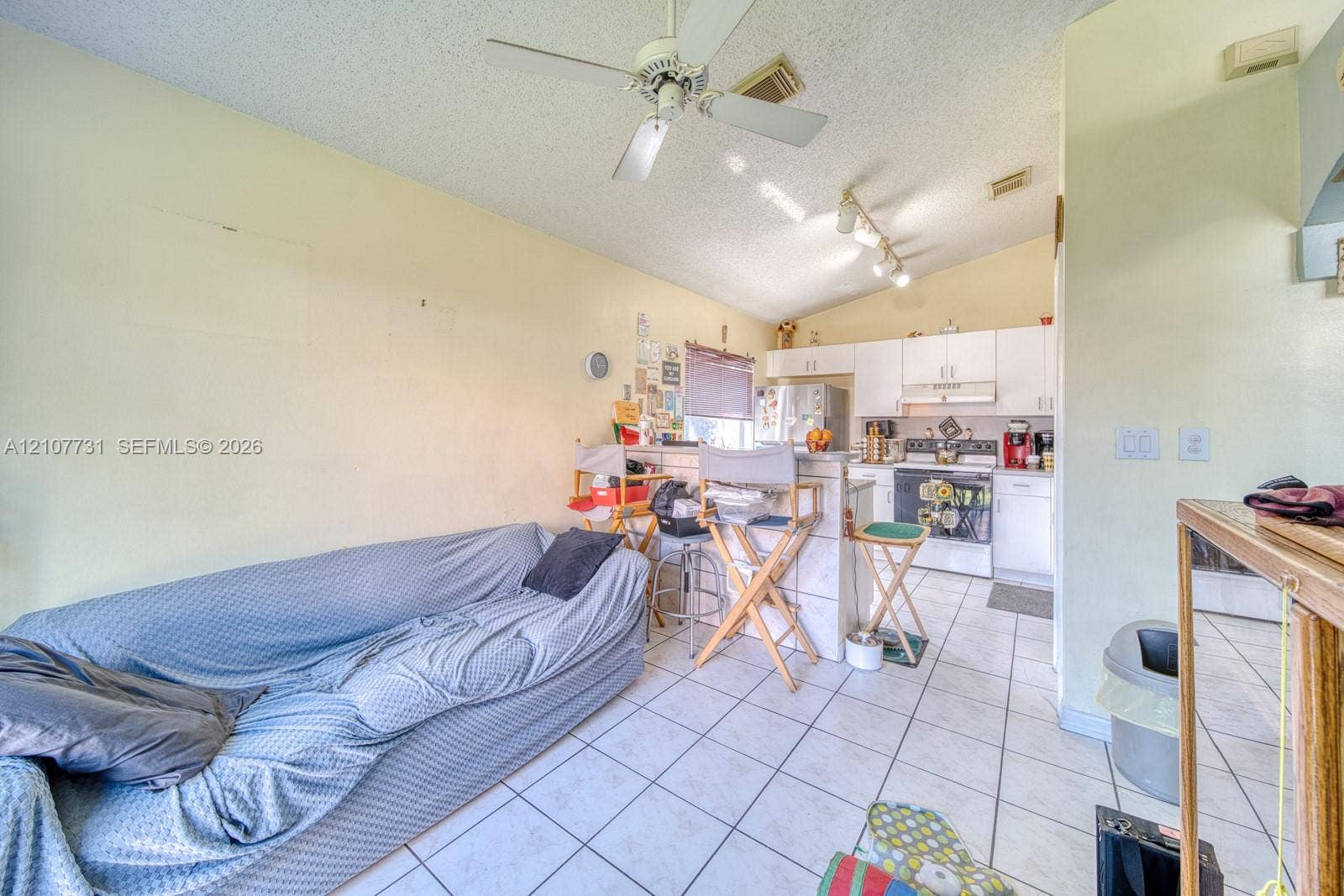 Vaulted ceiling with a central paddle fan, white cabinetry, tile flooring, and a raised kitchen island counter