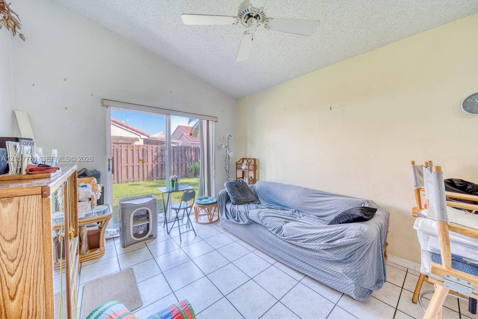 Vaulted ceiling with a white overhead fan, light-colored tile flooring, and a sliding glass door providing external access