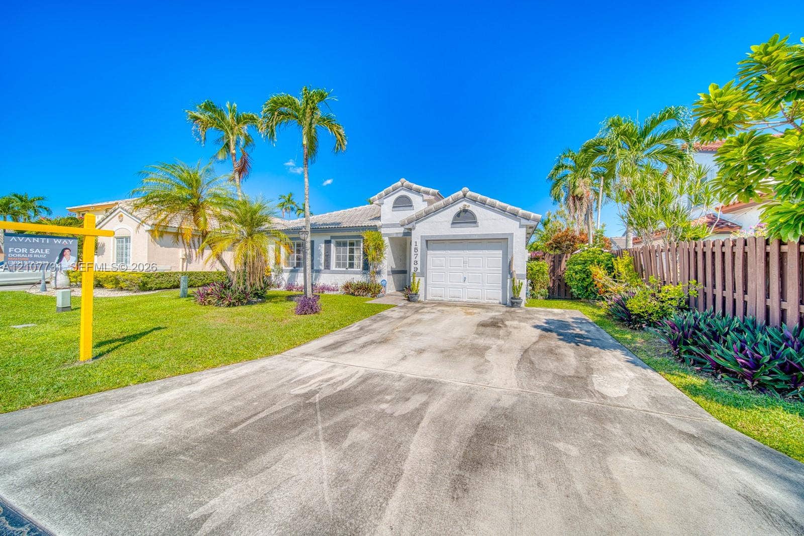 Single-story exterior featuring a concrete tile roof, attached one-car garage, concrete driveway, and mature landscaping