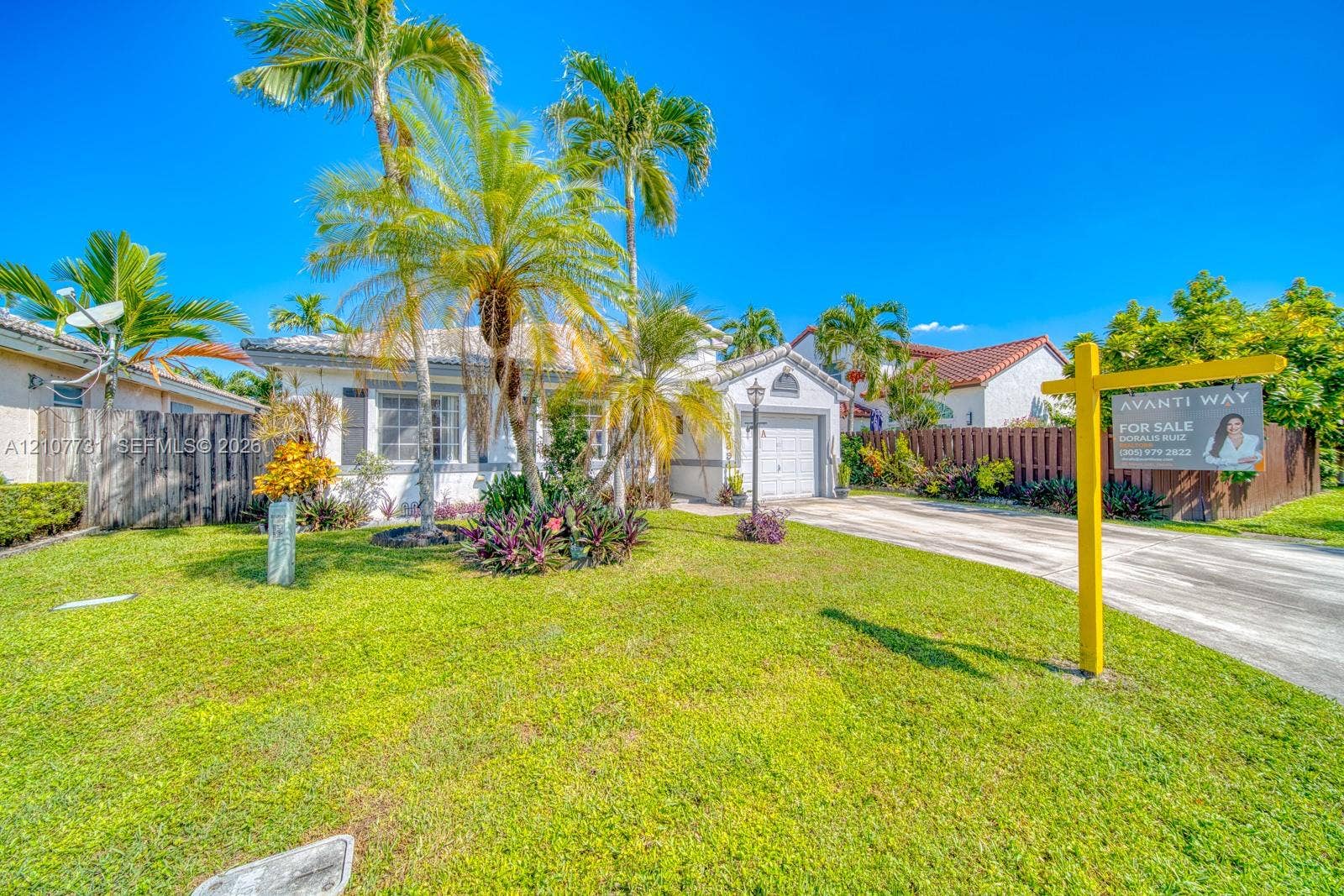Single-story residence featuring a tile roof, light-toned stucco exterior, integrated garage, and landscaped front yard with mature palm trees