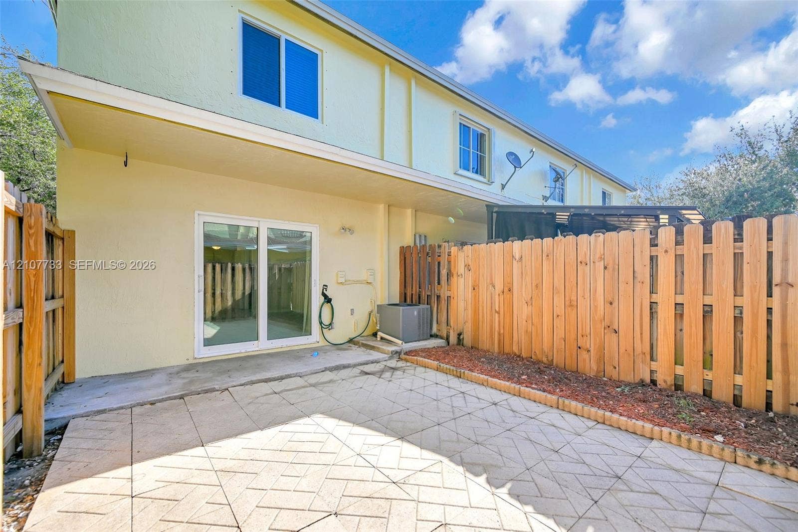 19606 SW 103rd Court, #4, Cutler Bay, FL 33157 Rear patio featuring patterned paver hardscaping, dual-panel sliding glass doors, and a wood privacy fence