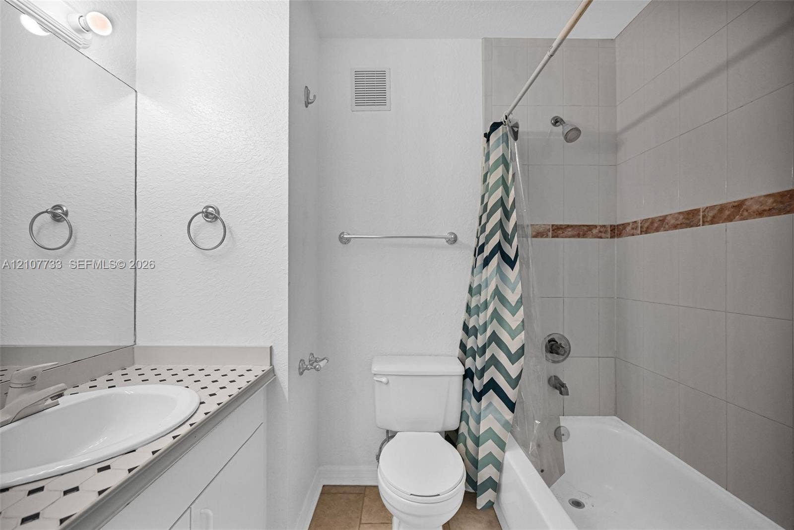 19606 SW 103rd Court, #4, Cutler Bay, FL 33157 Bathroom featuring a vanity with a patterned countertop, integrated basin, wall-to-wall mirror, and a tiled shower-tub combination with a decorative accent border