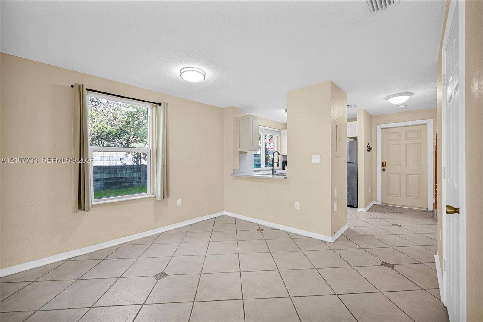 19606 SW 103rd Court, #4, Cutler Bay, FL 33157 Tile flooring set on a diagonal pattern, neutral wall color, oversized window, and kitchen pass-through with a light-toned countertop