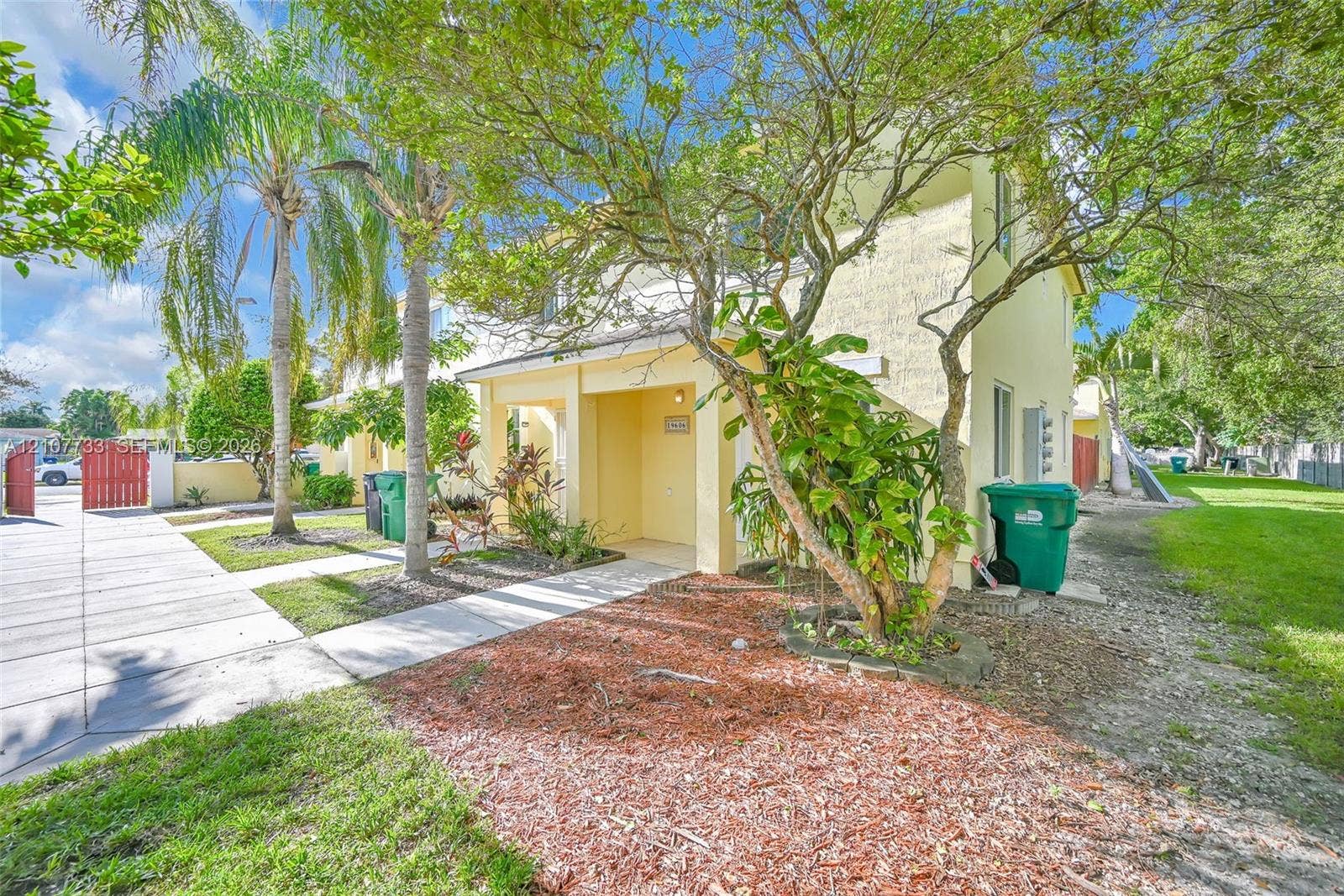 19606 SW 103rd Court, #4, Cutler Bay, FL 33157 Two-story exterior featuring a stucco facade, covered entryway, concrete walkway, and landscaped garden area with mulch beds and palm trees
