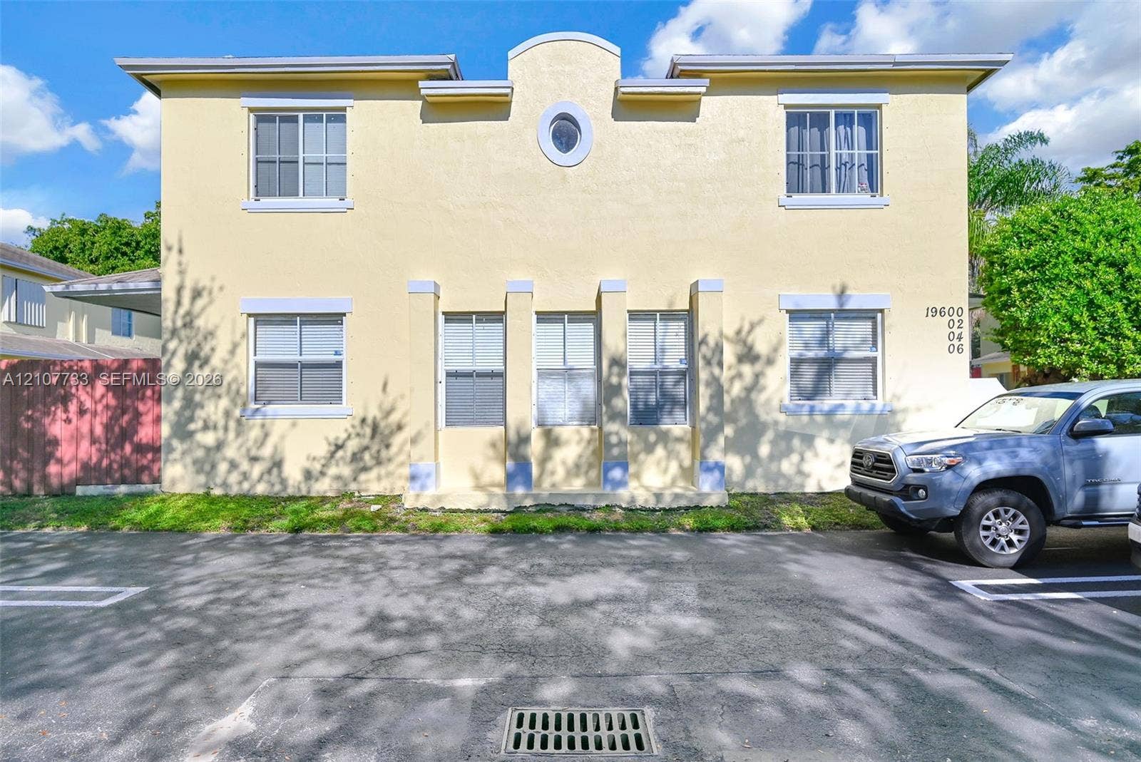 19606 SW 103rd Court, #4, Cutler Bay, FL 33157 Two-story exterior featuring a stucco finish, rhythmic vertical columns, an arched roofline parapet, a central oval window, and grid-patterned windows
