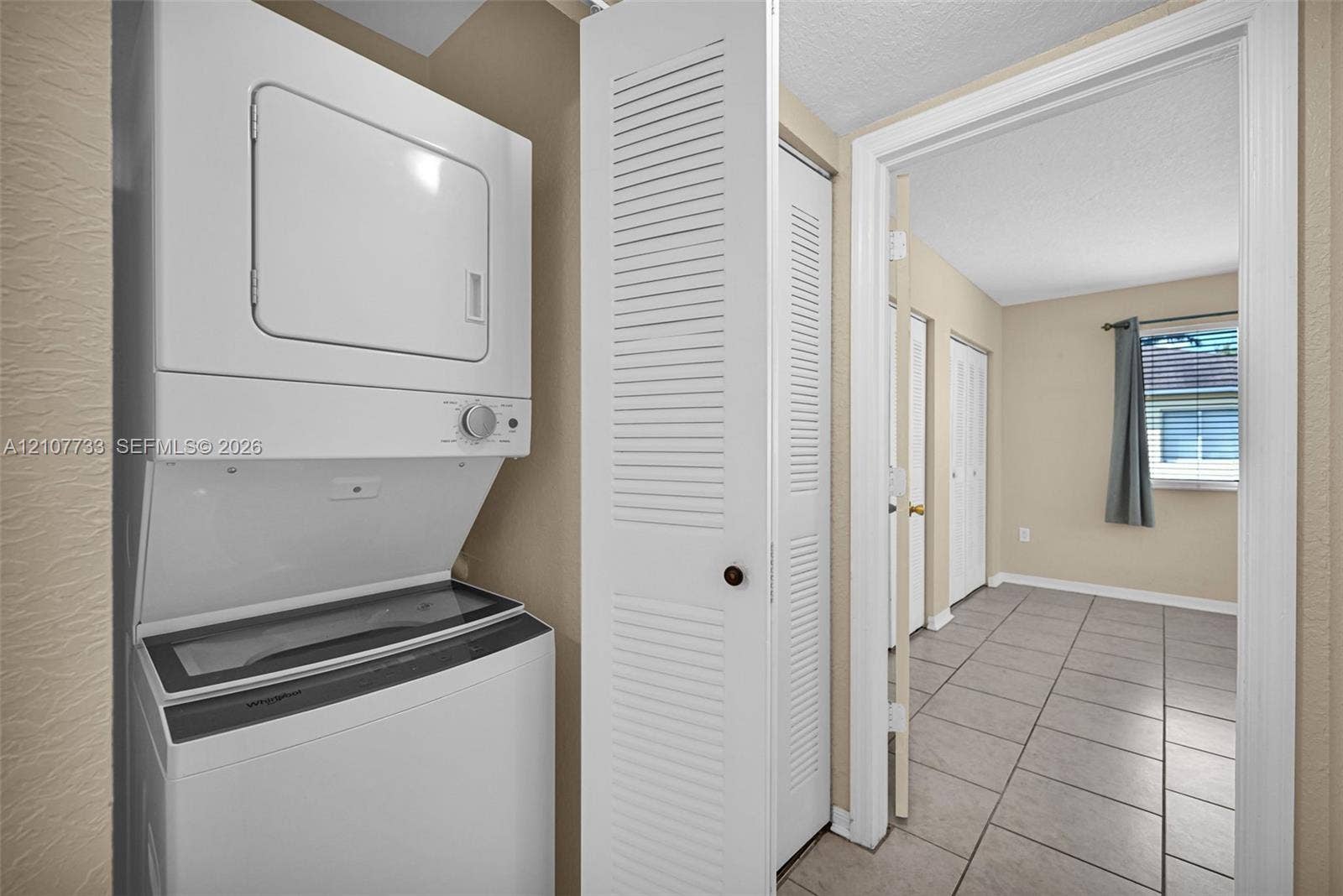 19606 SW 103rd Court, #4, Cutler Bay, FL 33157 Laundry area featuring a stacked washer and dryer unit, white louvered bi-fold closet doors, and ceramic tile flooring