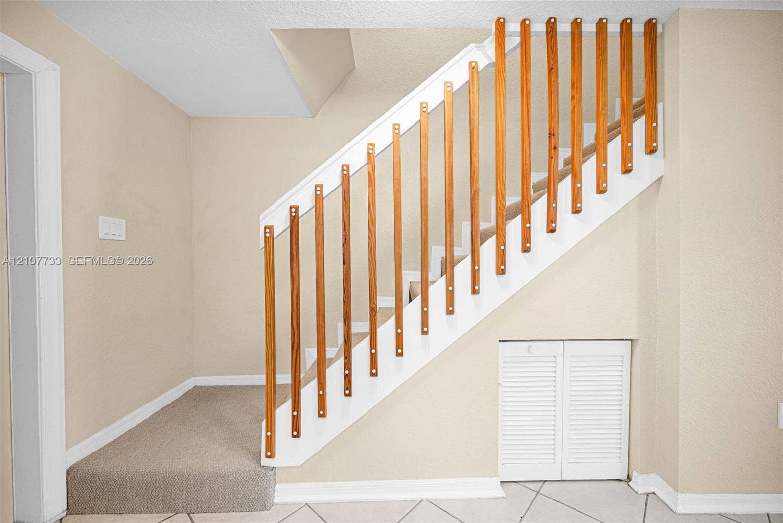 19606 SW 103rd Court, #4, Cutler Bay, FL 33157 Staircase featuring white painted stringers, natural wood vertical balusters, carpeted treads, and built-in louvered storage cabinetry