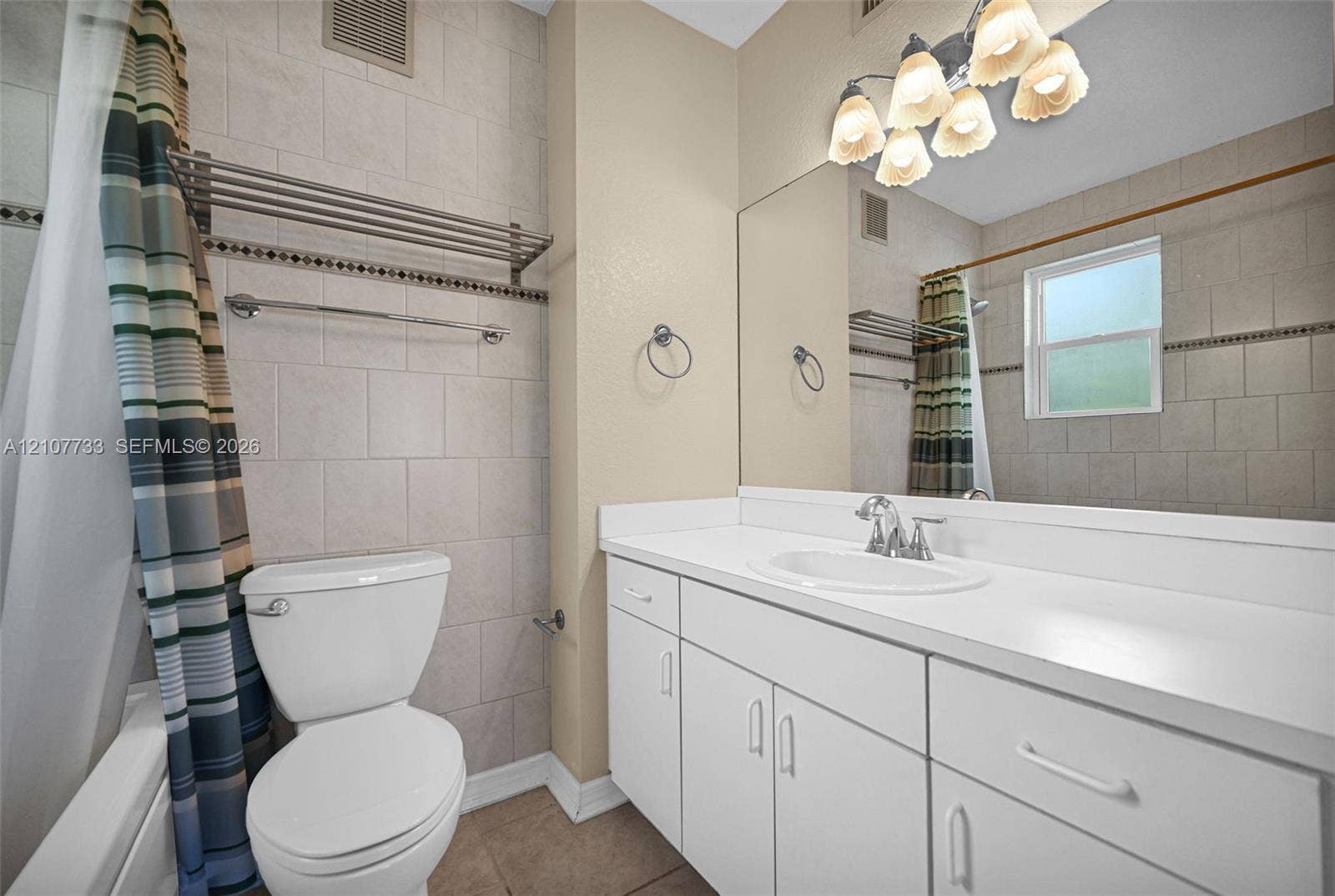 19606 SW 103rd Court, #4, Cutler Bay, FL 33157 Bathroom featuring a vanity with a white countertop and oval under-mount sink, full-width wall mirror, five-light fixture, and tile-surround tub area with decorative accent inlay