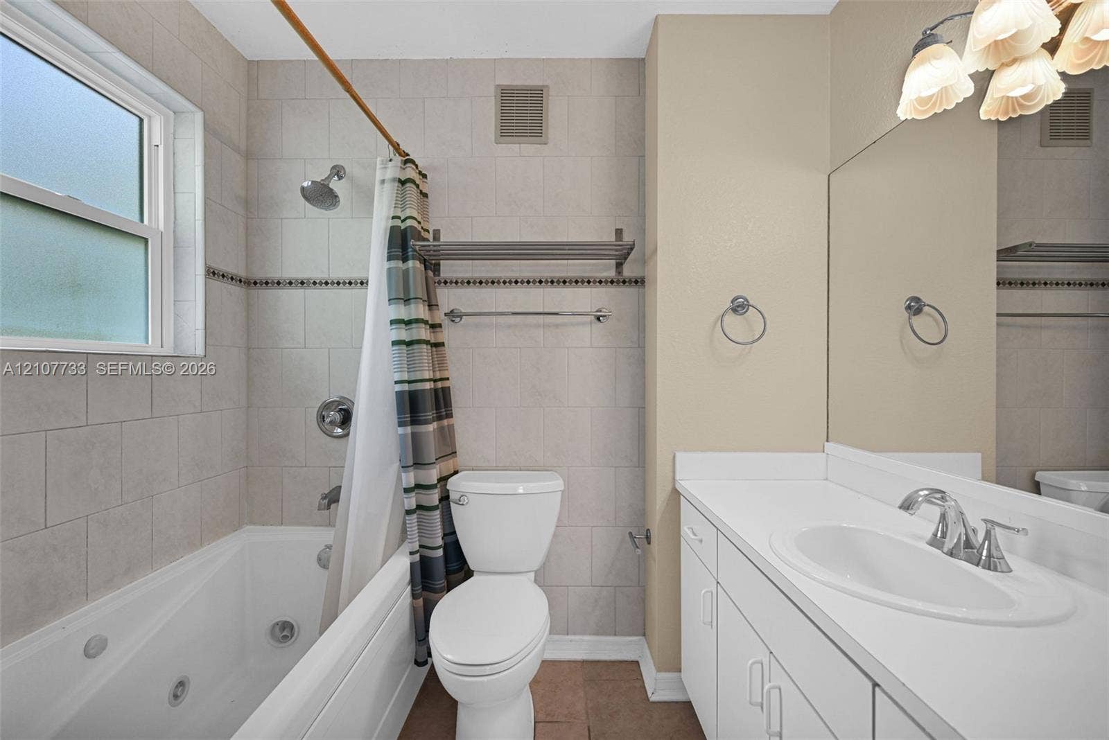 19606 SW 103rd Court, #4, Cutler Bay, FL 33157 Bathroom featuring a jetted soaking tub with a tiled surround, a white vanity with an integrated basin, a large wall-mounted mirror, and decorative wall lighting