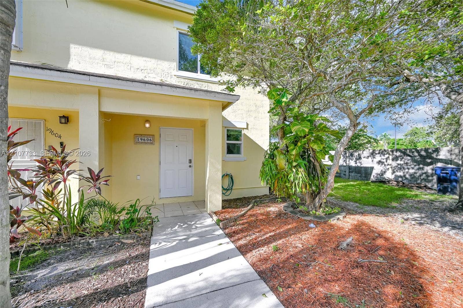 19606 SW 103rd Court, #4, Cutler Bay, FL 33157 Stucco exterior featuring a covered entryway, paved walkway, mature landscaping, and an external wall light fixture