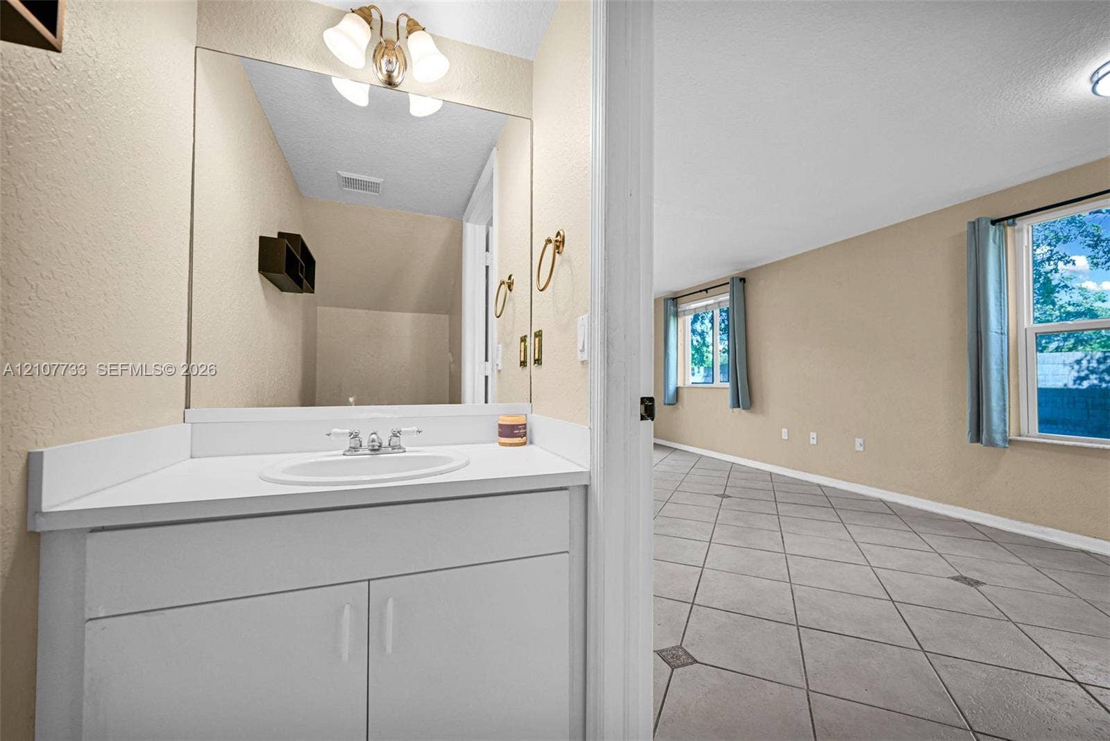 19606 SW 103rd Court, #4, Cutler Bay, FL 33157 Bathroom vanity featuring a white cabinet, solid-surface countertop with an integrated oval sink, and a large-format mirror with multi-bulb overhead lighting, complemented by tile flooring with decorative inserts