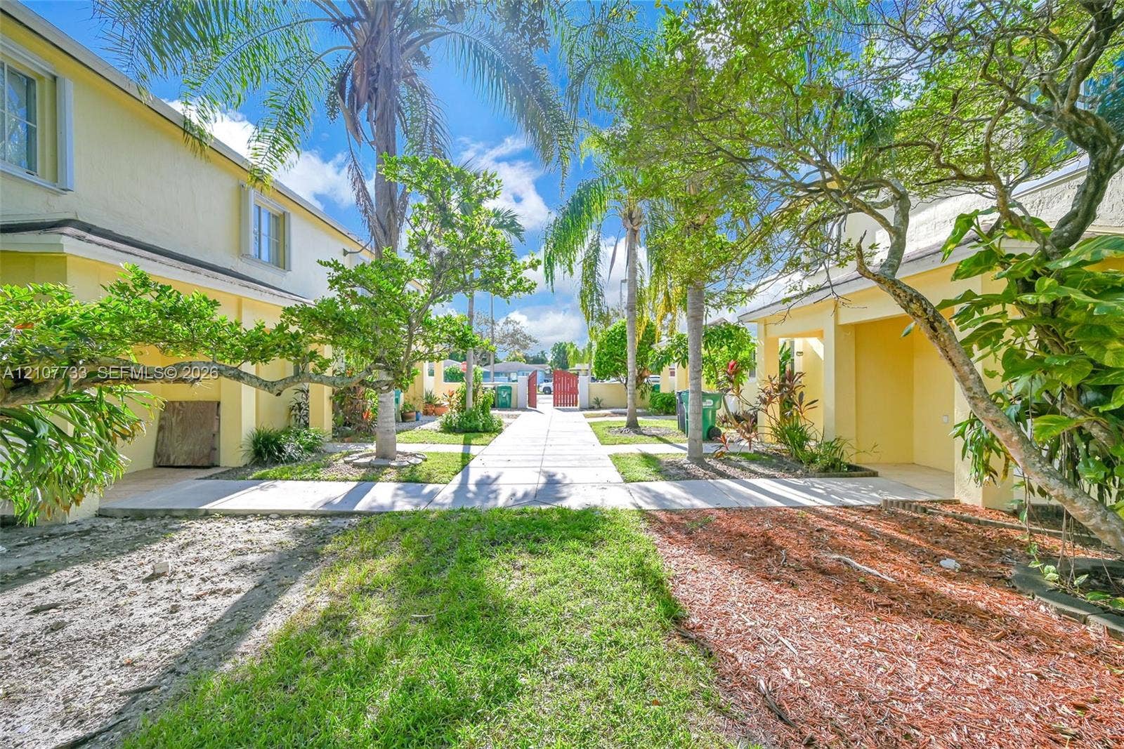 19606 SW 103rd Court, #4, Cutler Bay, FL 33157 Exterior courtyard featuring paved walkways, mature palm trees, stucco building siding, and metal gated access