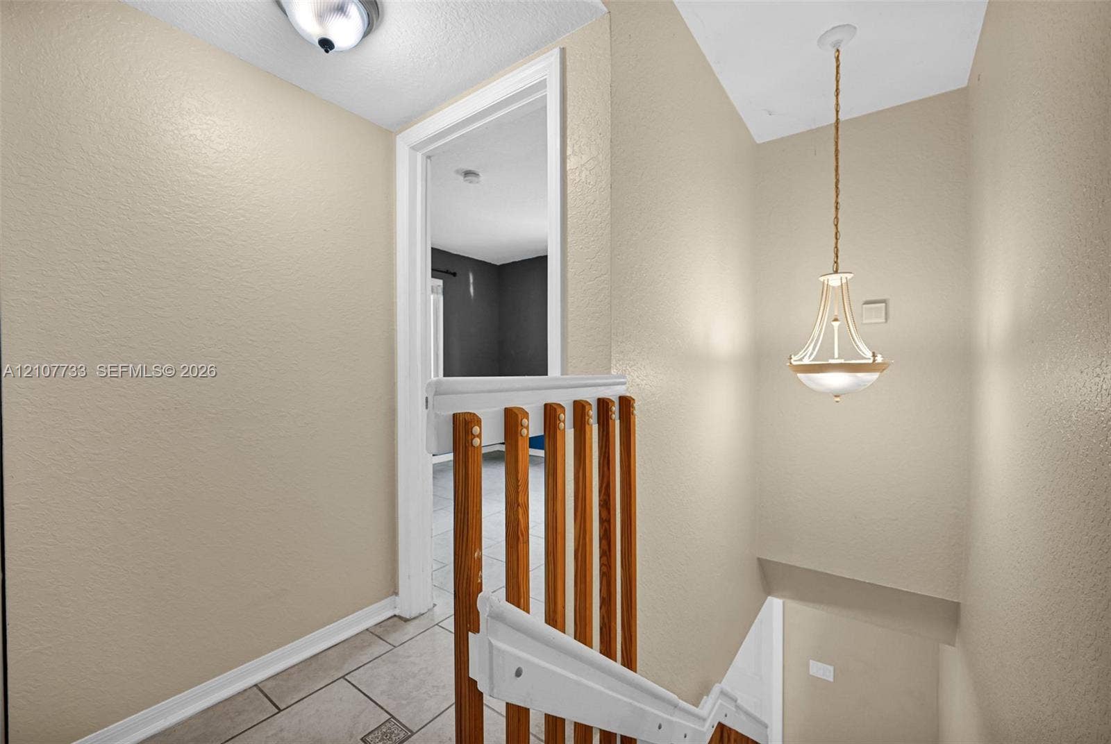 19606 SW 103rd Court, #4, Cutler Bay, FL 33157 Staircase featuring wood-slat railings, a decorative metal pendant light fixture, ceiling-mounted dome lighting, and neutral tile flooring