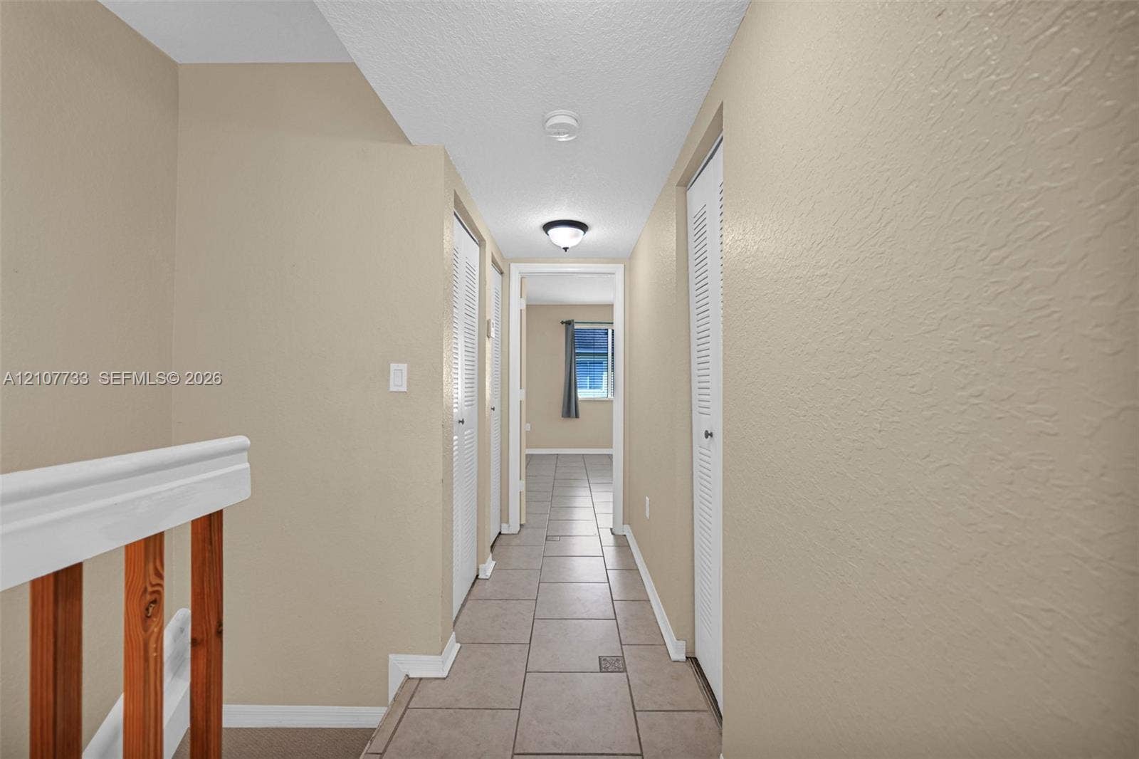19606 SW 103rd Court, #4, Cutler Bay, FL 33157 Hallway featuring large-format ceramic tile flooring, neutral wall tones, dual bi-fold closet doors, and wood-finish railing accents