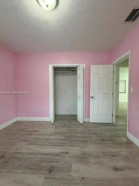Wood-finish flooring, six-panel interior door, and closet featuring overhead storage shelving and a hanging rod