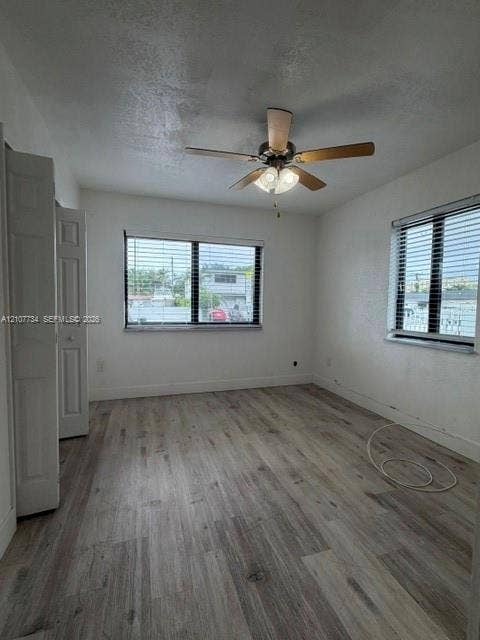 Interior room featuring wood-finish flooring, two dual-pane windows with horizontal blinds, a ceiling fan with integrated lighting, and a bi-fold closet door
