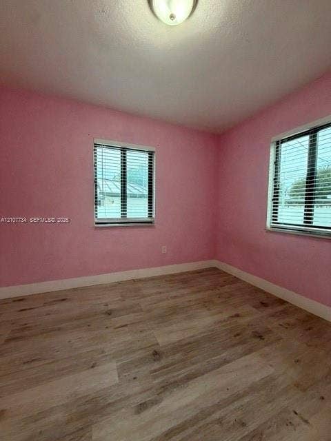 Room featuring wood-finish flooring, two windows with horizontal blinds, and a central ceiling-mounted light fixture