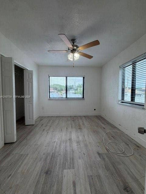Room featuring wood-finish flooring, a ceiling fan with integrated lighting, dual windows with horizontal blinds, and a double-door closet