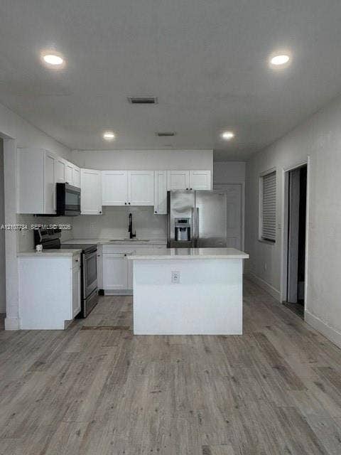 Kitchen featuring white cabinetry, quartz countertops, a central island, stainless steel appliances, and wood-finish flooring