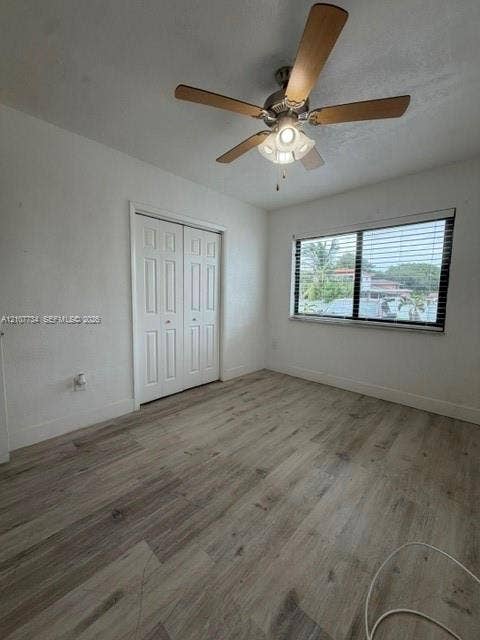 Room featuring wood-finish flooring, a ceiling fan with integrated lighting, and a double-door closet