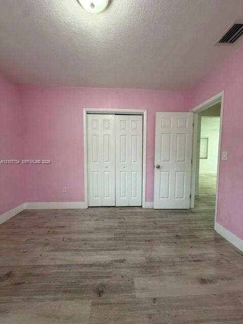 Room featuring wood-finish flooring, dual-panel closet doors, and a paneled entry door