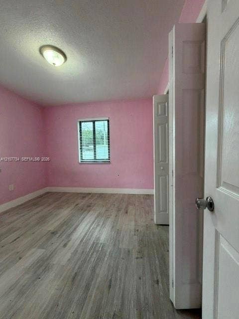 Room featuring wood-finish flooring, a single window, a ceiling-mounted light fixture, and a bi-fold closet door