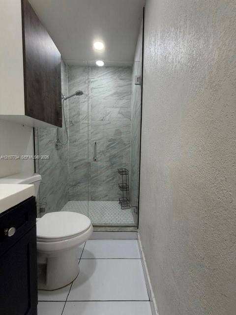 Walk-in shower with floor-to-ceiling stone-pattern tile, glass enclosure, and recessed lighting, paired with a dark-finish vanity featuring a white countertop and large-format floor tile