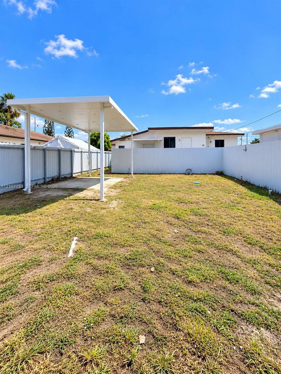 Fenced backyard featuring an expansive open lawn and a covered structural canopy with a concrete pad
