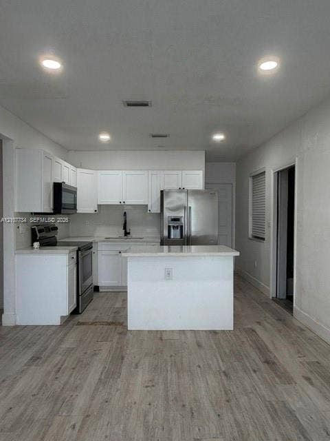 Kitchen featuring white shaker-style cabinetry, wood-finish flooring, recessed lighting, stainless steel appliances, and a central island with a stone-surface countertop