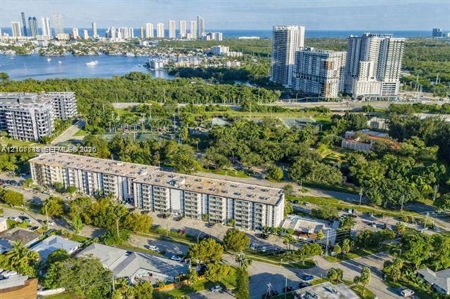Aerial perspective featuring a multi-story residential building, surrounding mature tree canopy, integrated paved parking areas, and proximity to regional parkland