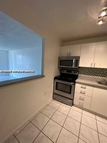 Kitchen featuring white flat-panel cabinetry, stainless steel appliances, a patterned tile backsplash, and light-toned tile flooring
