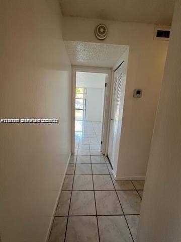 Hallway featuring light-colored tile flooring and a built-in closet with louvered doors