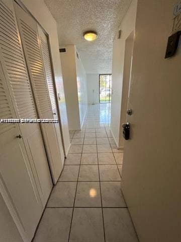 Hallway featuring white ceramic tile flooring, built-in louvered-door closets, and flush-mount lighting
