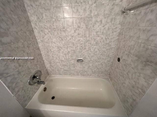 Bathtub enclosure featuring full-height ceramic wall tiling, polished chrome faucet, and integrated metal shower rod