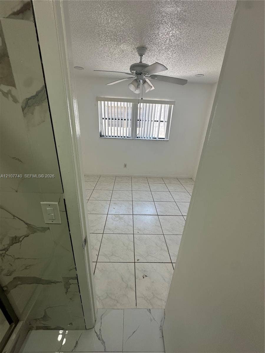 Large-format tile flooring, ceiling fan with integrated lighting, and vertical window blinds