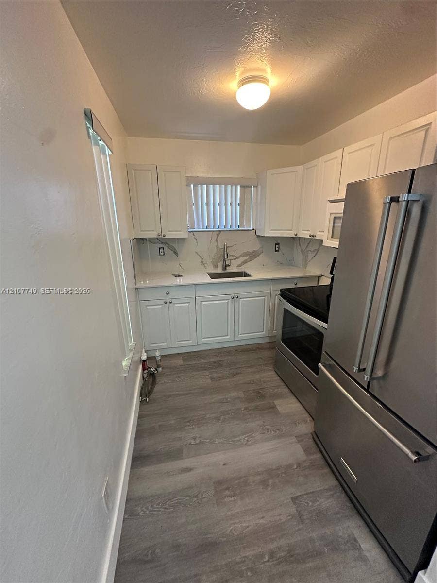 Kitchen featuring white cabinetry, stone-surface countertops with a decorative backsplash, stainless steel appliances, and wood-finish flooring