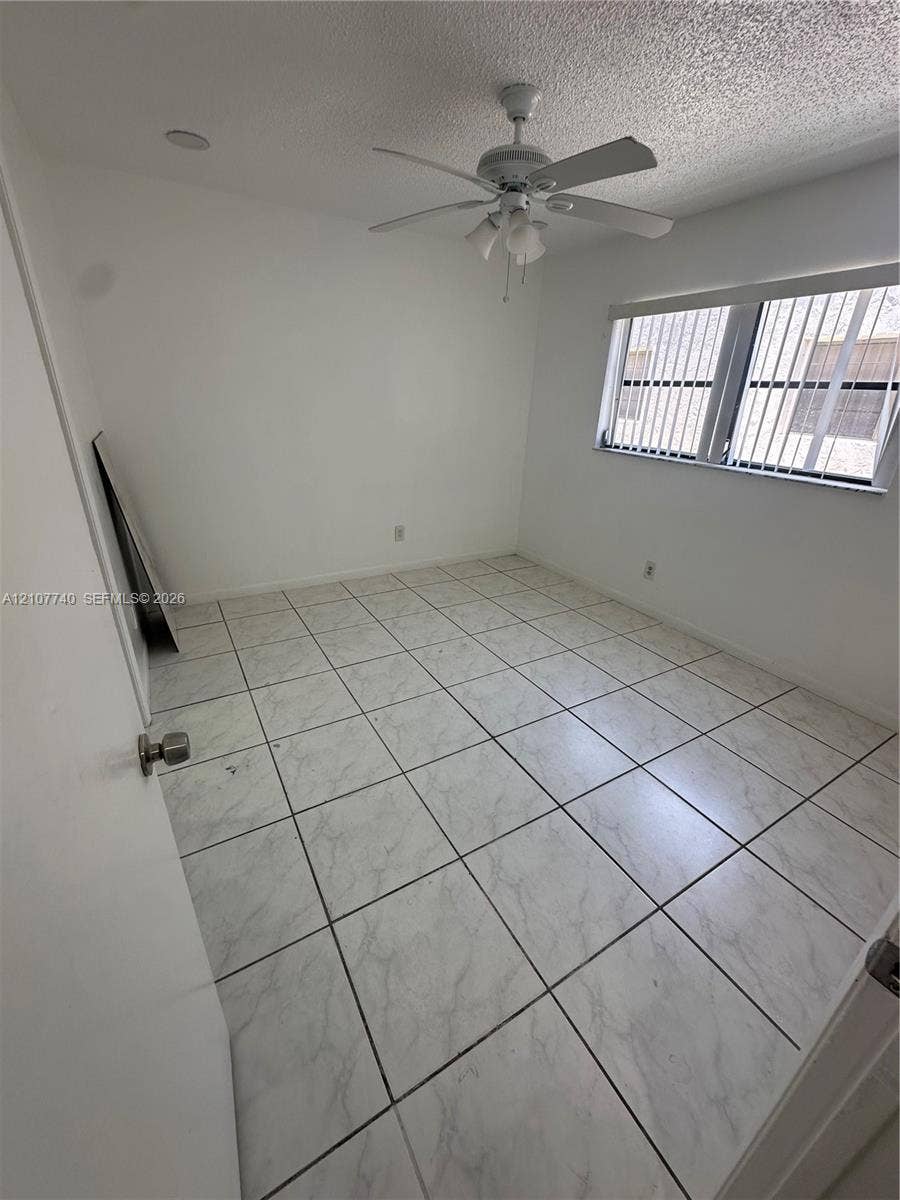 Room featuring large-format stone-patterned tile flooring, a multi-blade ceiling fan with integrated lighting, and a window with horizontal blinds