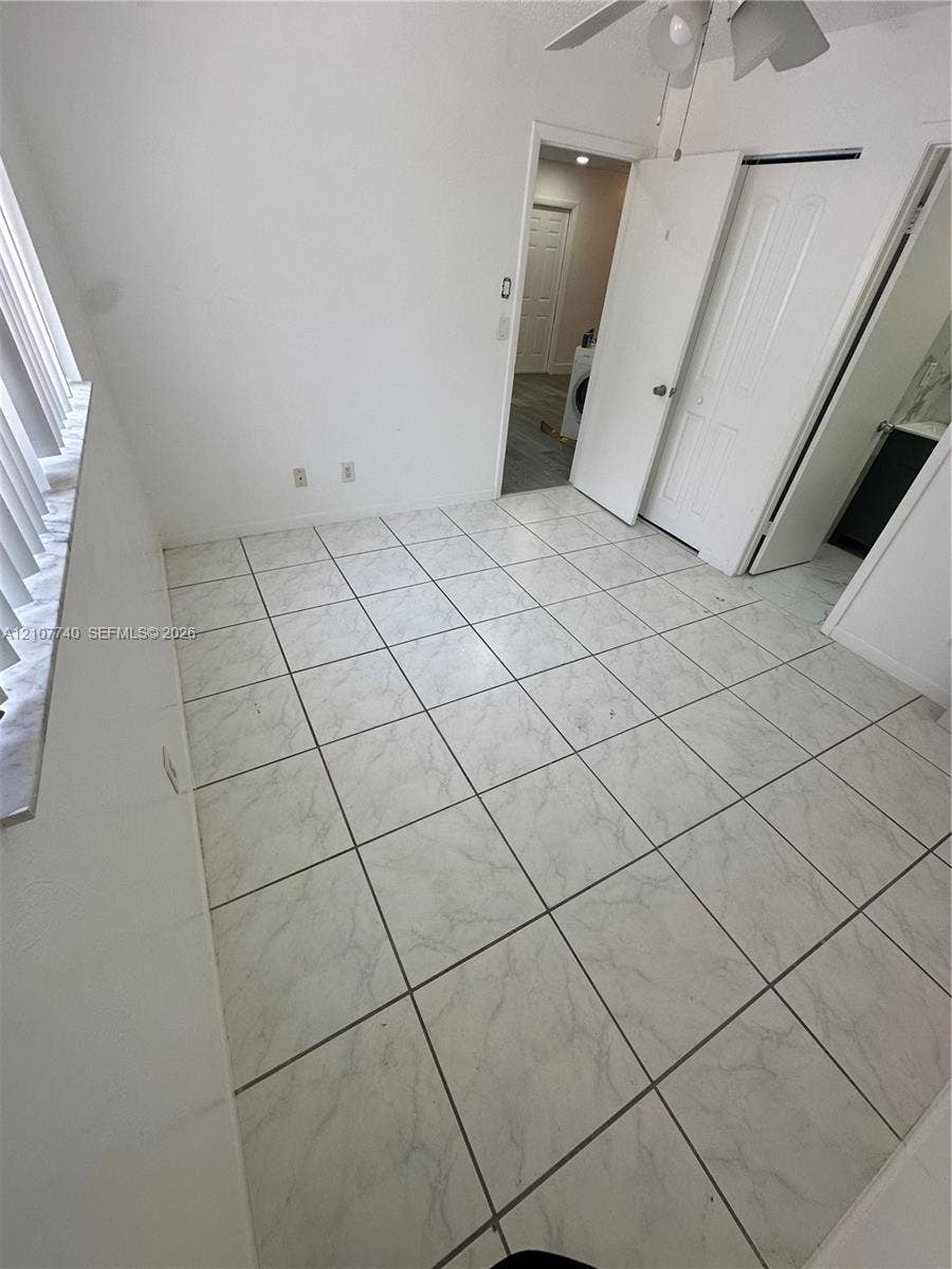 Neutral ceramic tile flooring, ceiling fan with integrated lighting, multi-panel doors, and vertical window blinds