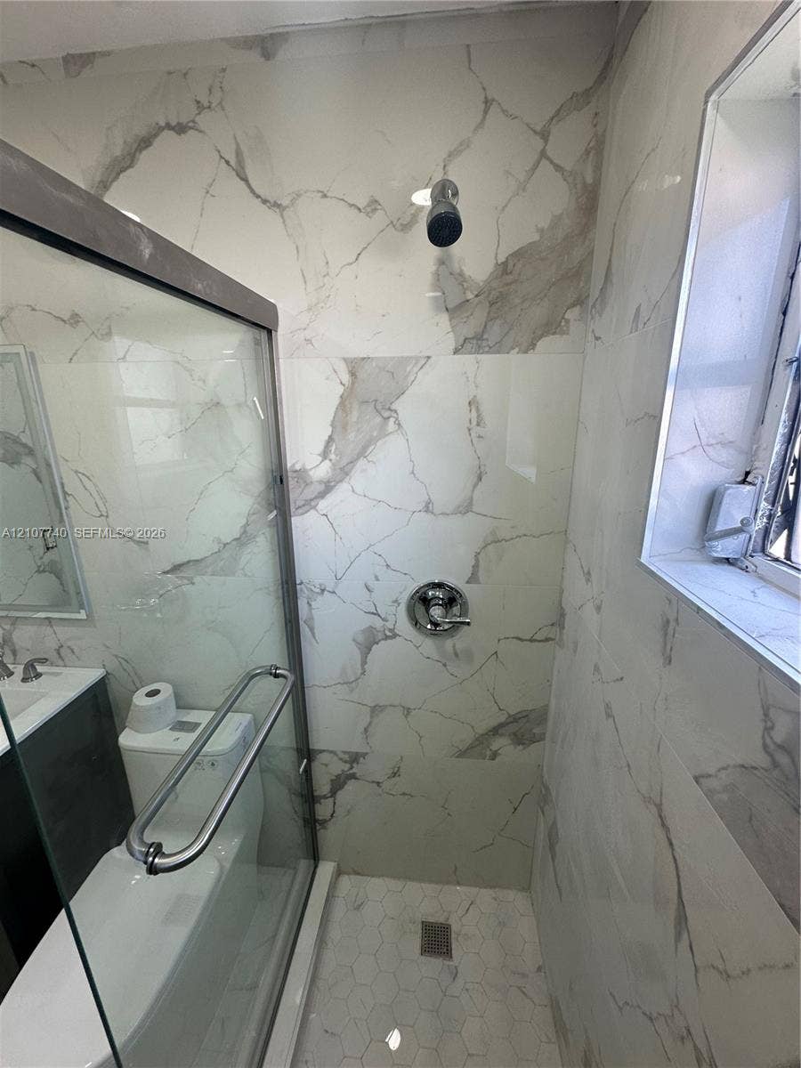 Shower featuring large-format wall tiles with veining patterns, glass enclosure with metal hardware, polished chrome shower fixtures, and hexagonal floor tiling