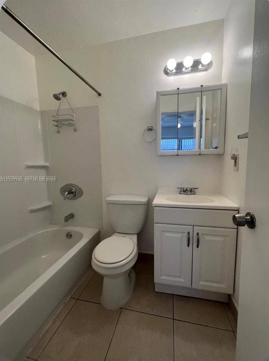 Bathroom featuring a white vanity cabinet with an integrated sink, a three-light wall fixture, a mirrored medicine cabinet, and a bathtub with a shower surround and tile flooring