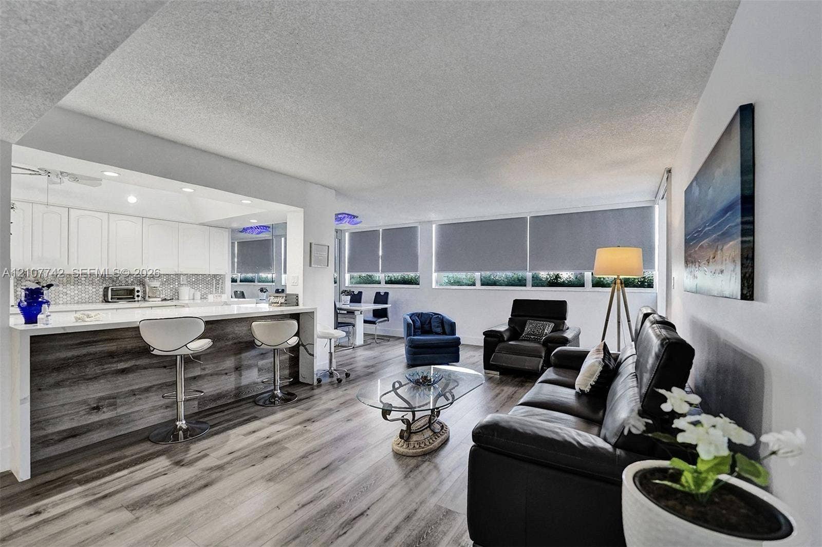100 Golden Isles Drive, #112, Hallandale Beach, Hallandale Beach, FL 33009 Open-concept interior featuring wood-finish flooring, a kitchen peninsula with bar seating, white cabinetry, a mosaic backsplash, and expansive windows