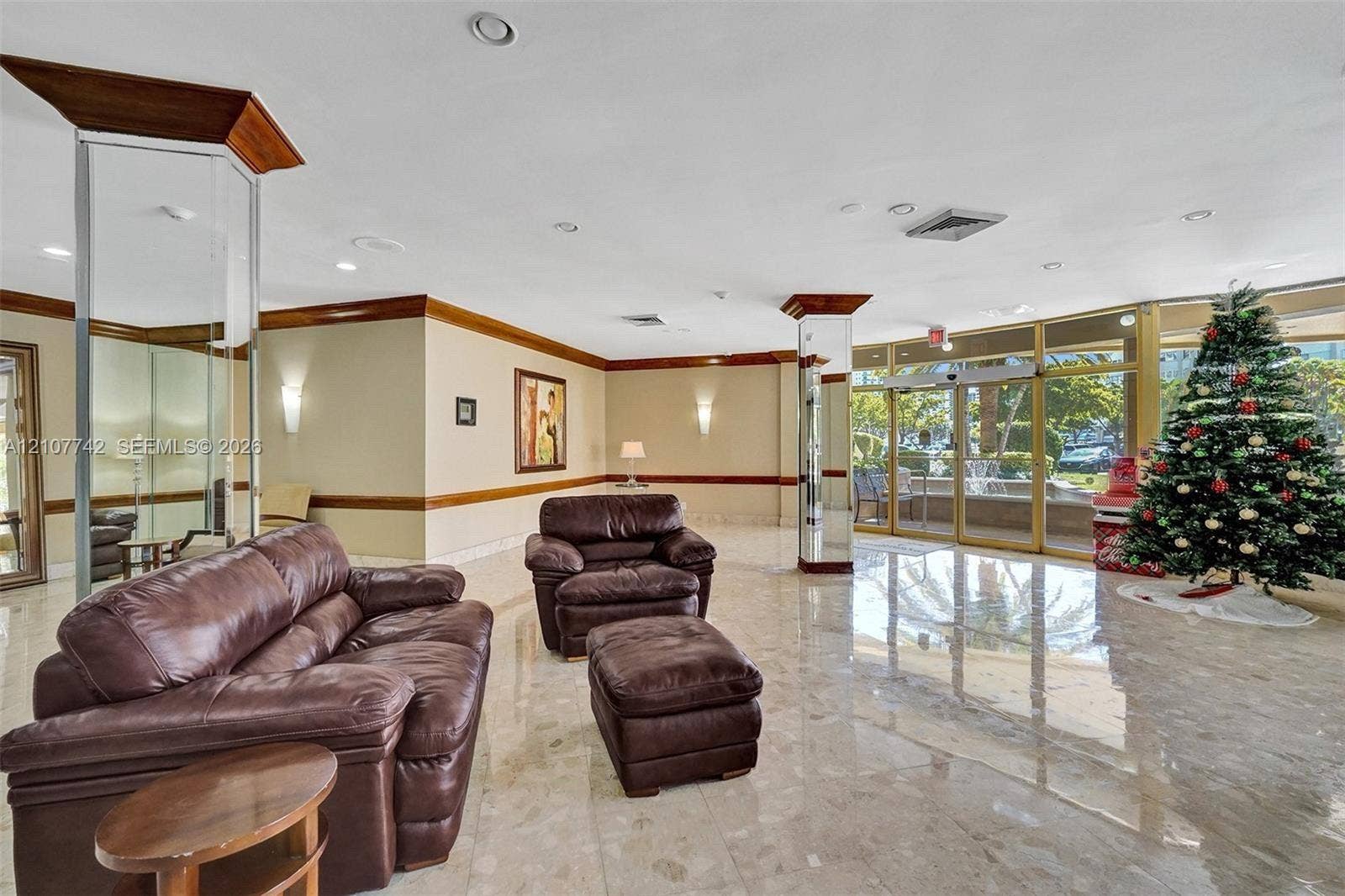100 Golden Isles Drive, #112, Hallandale Beach, Hallandale Beach, FL 33009 Common area lobby featuring polished stone flooring, mirrored structural columns, crown molding, and floor-to-ceiling glass panel walls
