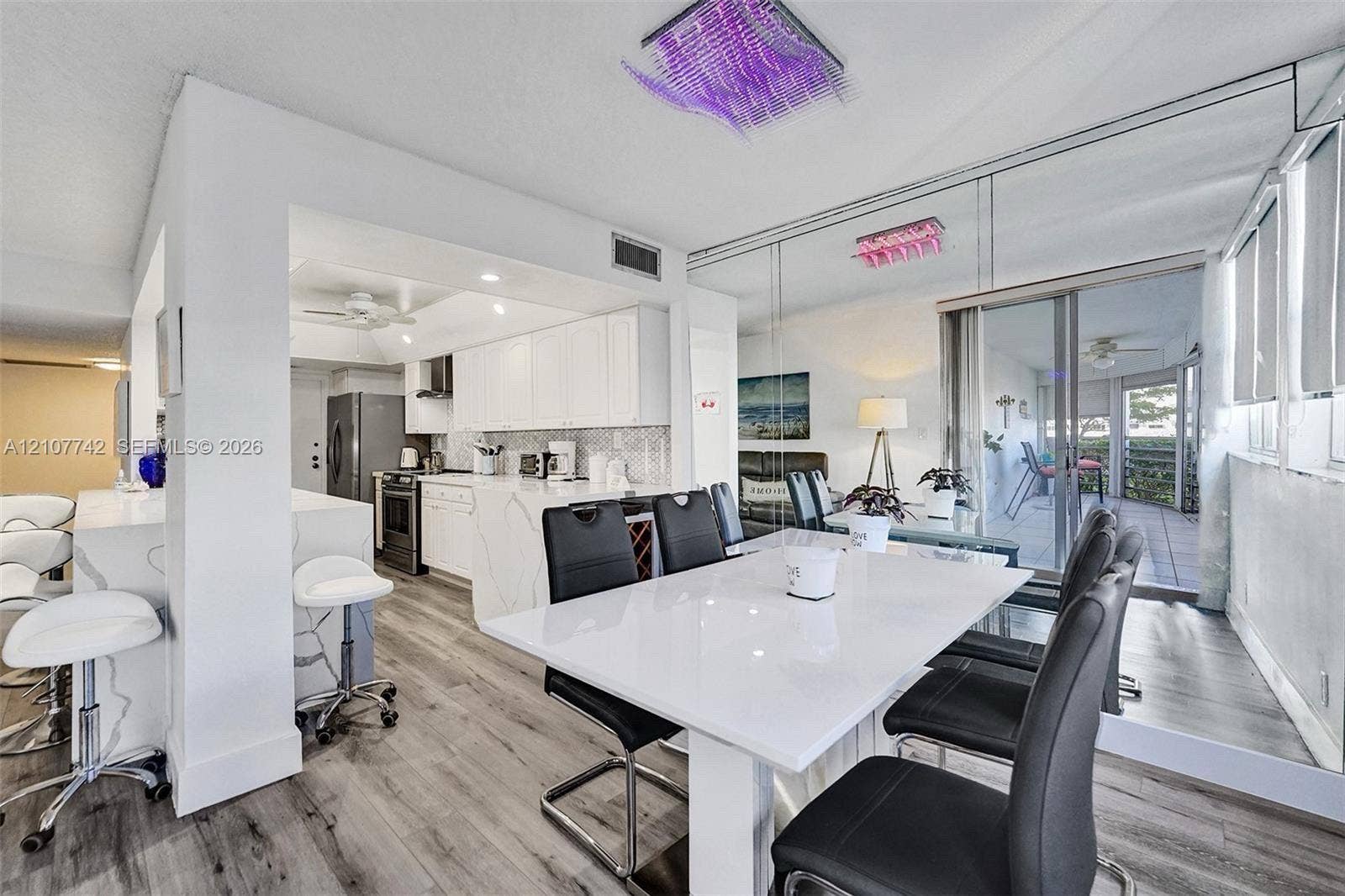 100 Golden Isles Drive, #112, Hallandale Beach, Hallandale Beach, FL 33009 Kitchen featuring white shaker cabinetry, stone-finish waterfall edge peninsula, stainless steel appliances, wood-finish flooring, and mirrored wall accents