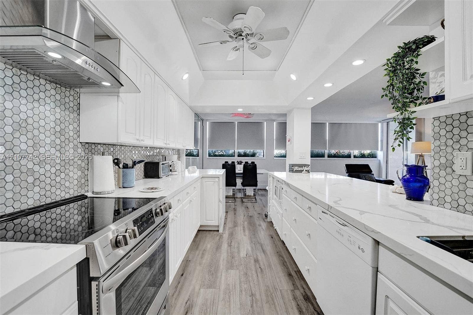 100 Golden Isles Drive, #112, Hallandale Beach, Hallandale Beach, FL 33009 Kitchen featuring white cabinetry, stone-finish countertops, hexagonal tile backsplash, stainless steel range with overhead ventilation, and wood-finish flooring