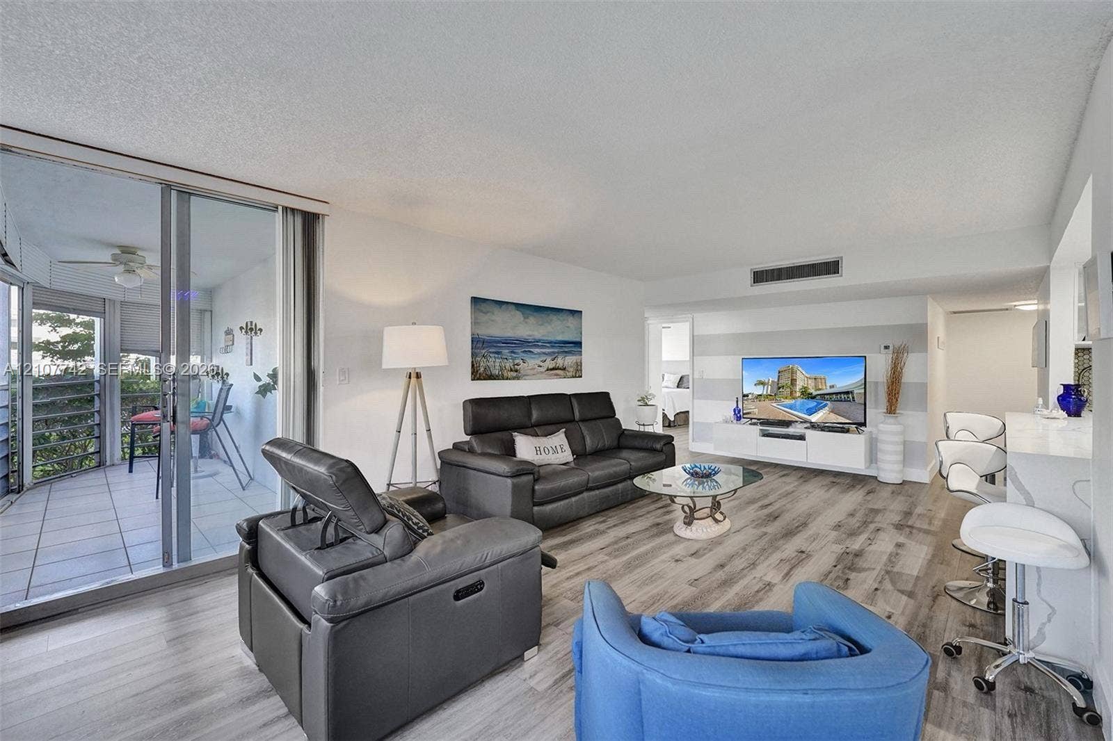 100 Golden Isles Drive, #112, Hallandale Beach, Hallandale Beach, FL 33009 Living area featuring wood-finish flooring, a built-in media console, a breakfast bar with stone-finish countertop, and floor-to-ceiling glass sliding doors opening to a private balcony