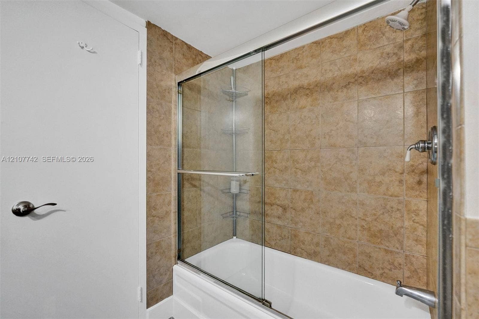100 Golden Isles Drive, #112, Hallandale Beach, Hallandale Beach, FL 33009 Bathtub with a glass sliding enclosure, metallic fixtures, and tiled wall surround featuring built-in corner shelving