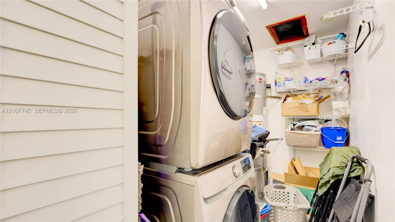 Stacked high-efficiency laundry appliances, louvered closet door, and tiered wire shelving