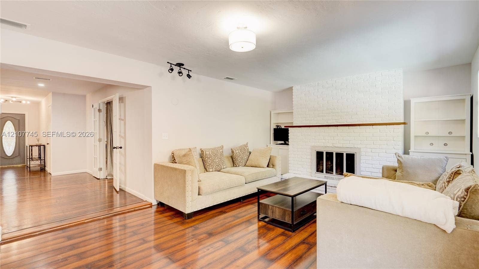 Living area featuring wood-finish flooring, a painted brick fireplace, built-in shelving, and recessed ceiling lighting